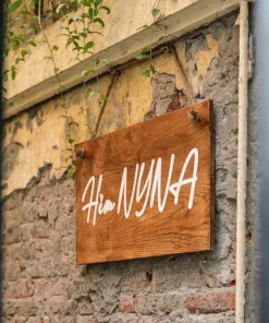 Bảng hiệu gỗ Hẻm Nina phong cách mộc mạc, chất liệu gỗ tự nhiên, nền tường gạch cổ điển.