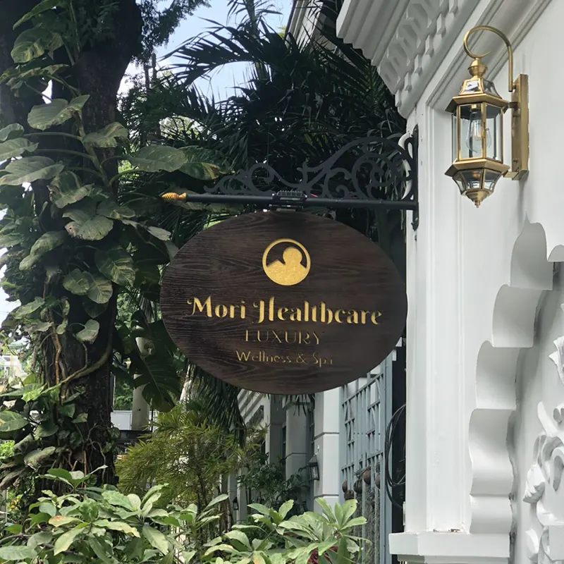 Bảng hiệu gỗ ngoài trời Mori Healthcare treo tròn, thiết kế tối giản giữa không gian xanh