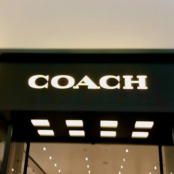 Bảng hiệu mica COACH với chữ nổi trắng sang trọng trên nền đen, thiết kế tối giản chuẩn phong cách thương hiệu cao cấp