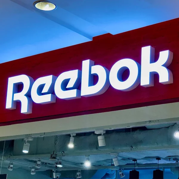 Bảng hiệu mica chữ nổi Reebok màu trắng trên nền đỏ, thiết kế hiện đại, thi công tại mặt tiền cửa hàng thể thao